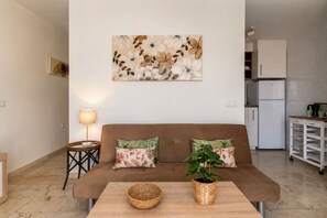 A living room with a brown sofa, two patterned cushions, a wall-mounted painting, a floor lamp, a small side table, a woven basket, and a potted plant. - GuestReady - Bright Stay with Balcony (Caleta de Fuste)