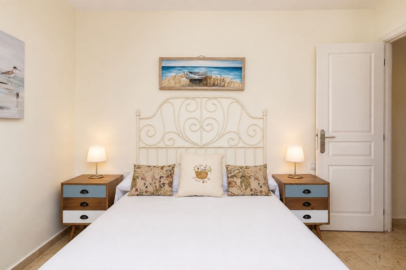 Un dormitorio con una cama, dos mesitas de noche, una puerta y un cuadro en la pared.