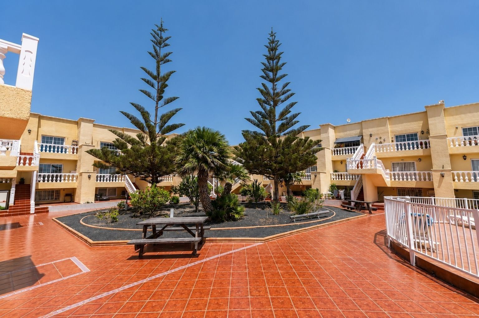 A courtyard with a tiled floor, a picnic table, and two tall trees.