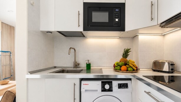 Een compacte keuken met een ingebouwde wasmachine, een magnetron en een broodrooster.
