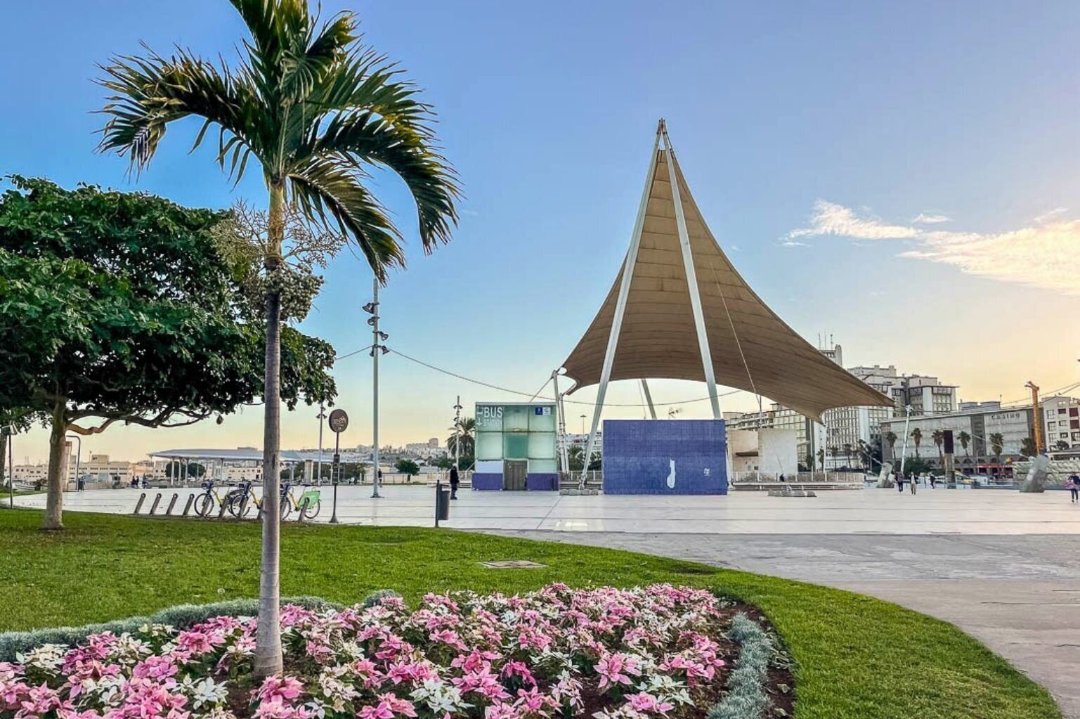 A public square with a modern pavilion, a bus stop, and a flower garden.