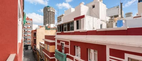 A narrow urban street with red and white buildings, a tall cylindrical structure, and a clear blue sky.