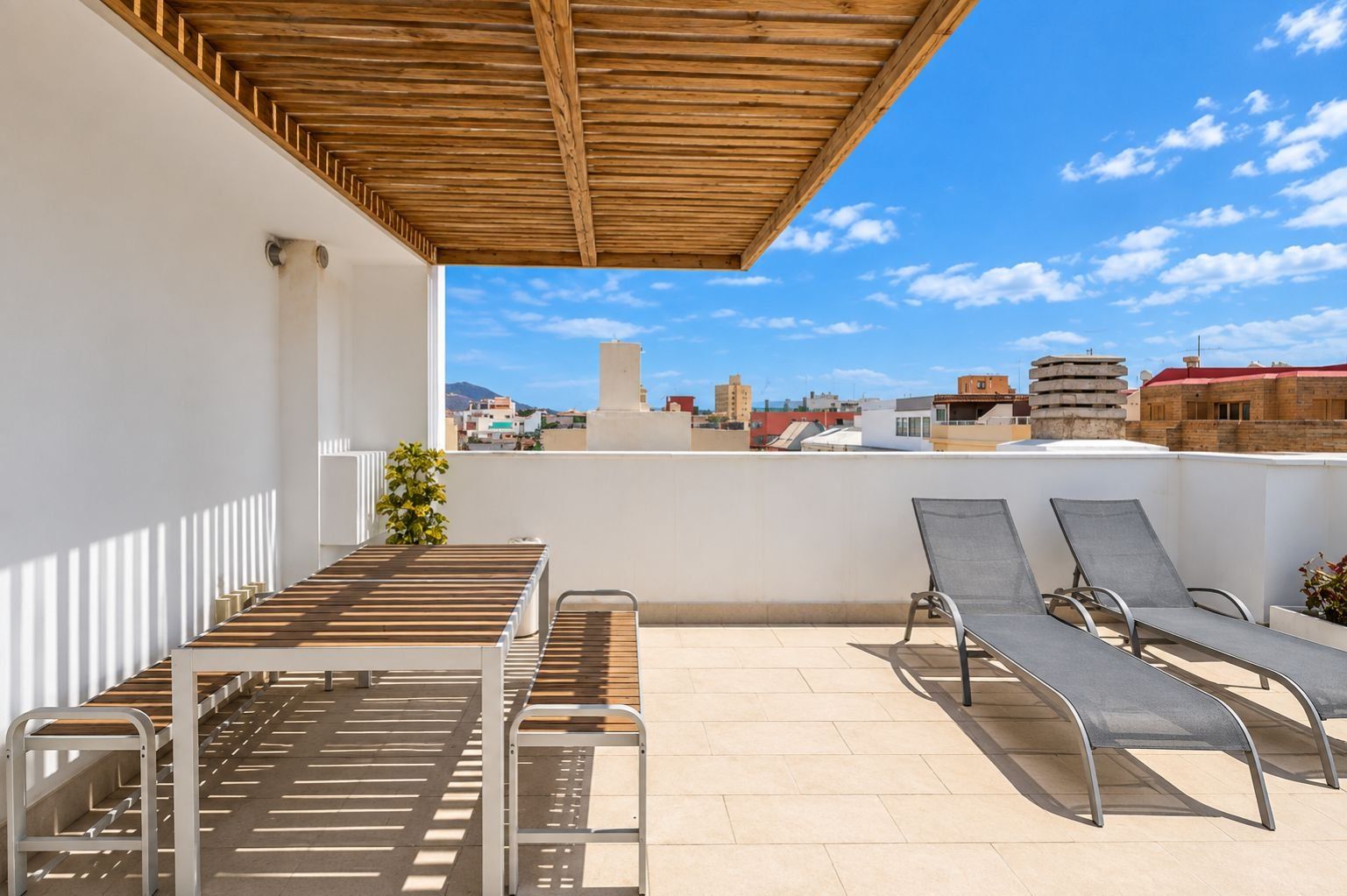 Eine Dachterrasse mit einer Holz-Pergola, einem Tisch und zwei Liegestühlen.