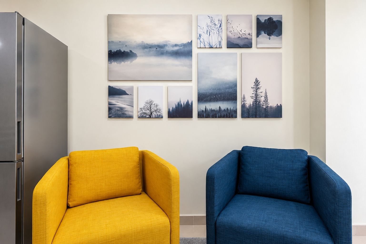 A room with a modern kitchen, two armchairs, and a wall with six landscape paintings.