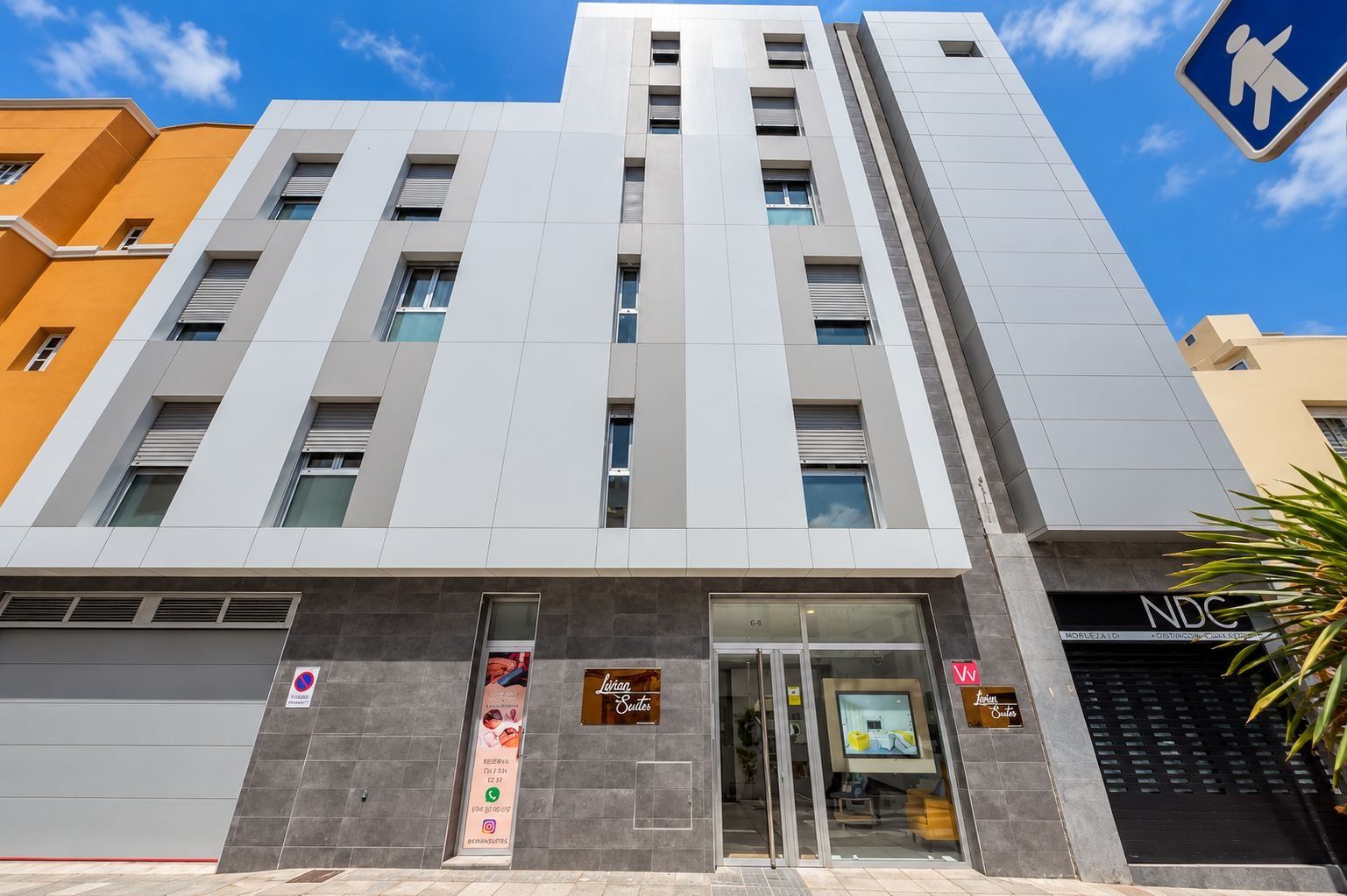 Un bâtiment moderne avec une entrée en verre, un panneau indiquant un passage piéton et une enseigne pour « Lujan Suites ».