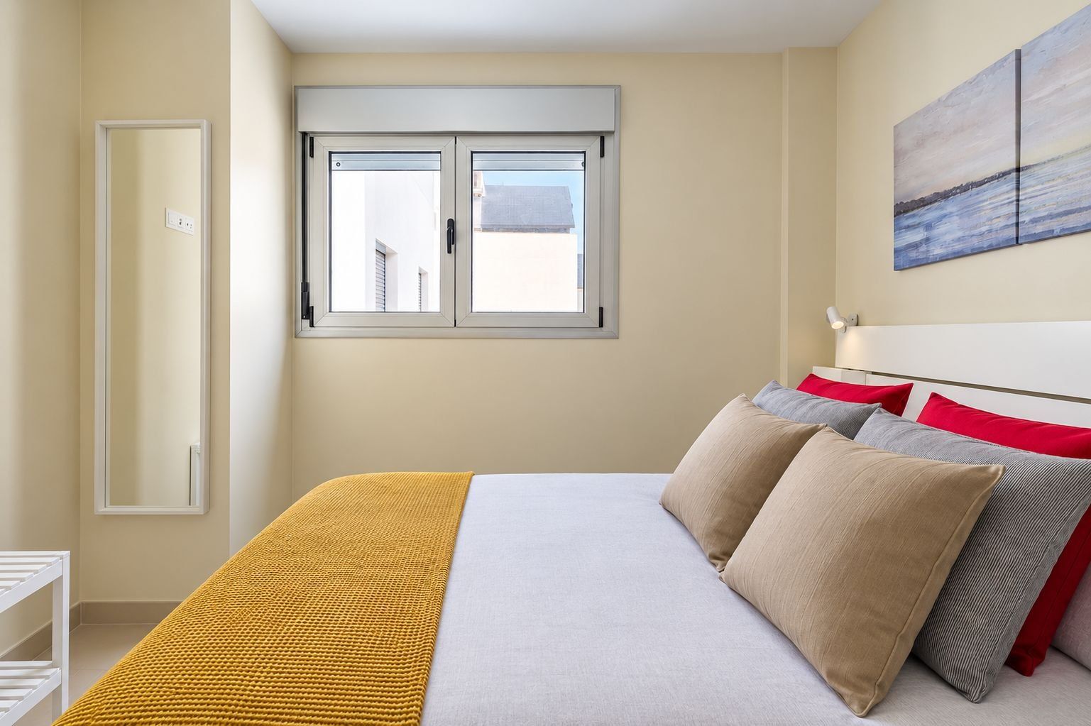 Ein Schlafzimmer mit einem Bett, Kissen, einem Fenster und einem Bild an der Wand.
