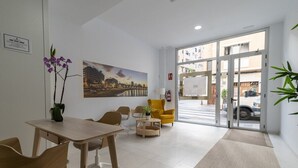 En hotellobby med en receptionsdisk, en sittgrupp, ett stort fönster med utsikt över staden och en dörr som leder ut.