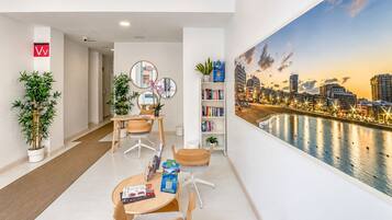 A modern hotel room with a cityscape view, a dining area with a table and chairs, and a bookshelf with books.