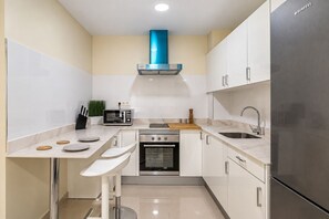 Cocina compacta con gabinetes blancos, un refrigerador de acero inoxidable, un microondas y un horno.