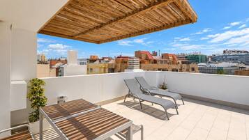 A rooftop terrace with a wooden pergola, two lounge chairs, a small table, and a potted plant.