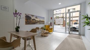 A hotel lobby with a reception desk, seating area, a large window with a cityscape view, and a door leading outside.