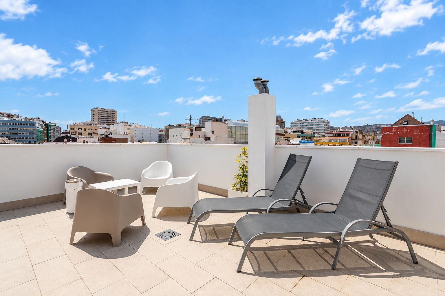 A rooftop terrace with lounge chairs, a table, and a white pillar.
