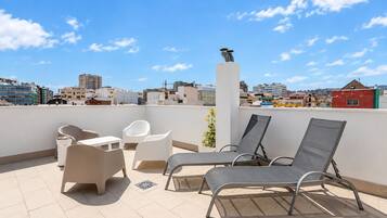 A rooftop terrace with lounge chairs, a table, and a white pillar.