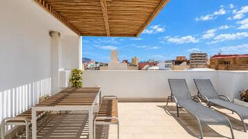 A rooftop terrace with a wooden pergola, a table, and two lounge chairs.