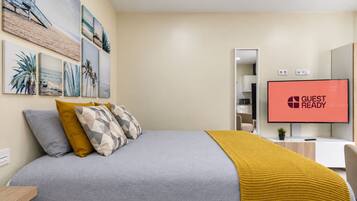 A hotel room with a bed, a TV displaying 'GUEST READY', and a wall with framed artwork.