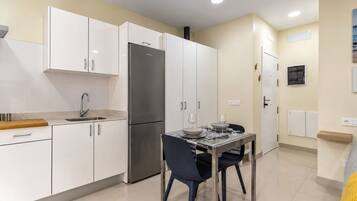 A modern kitchen with white cabinets, a stainless steel refrigerator, and a dining table set for two.