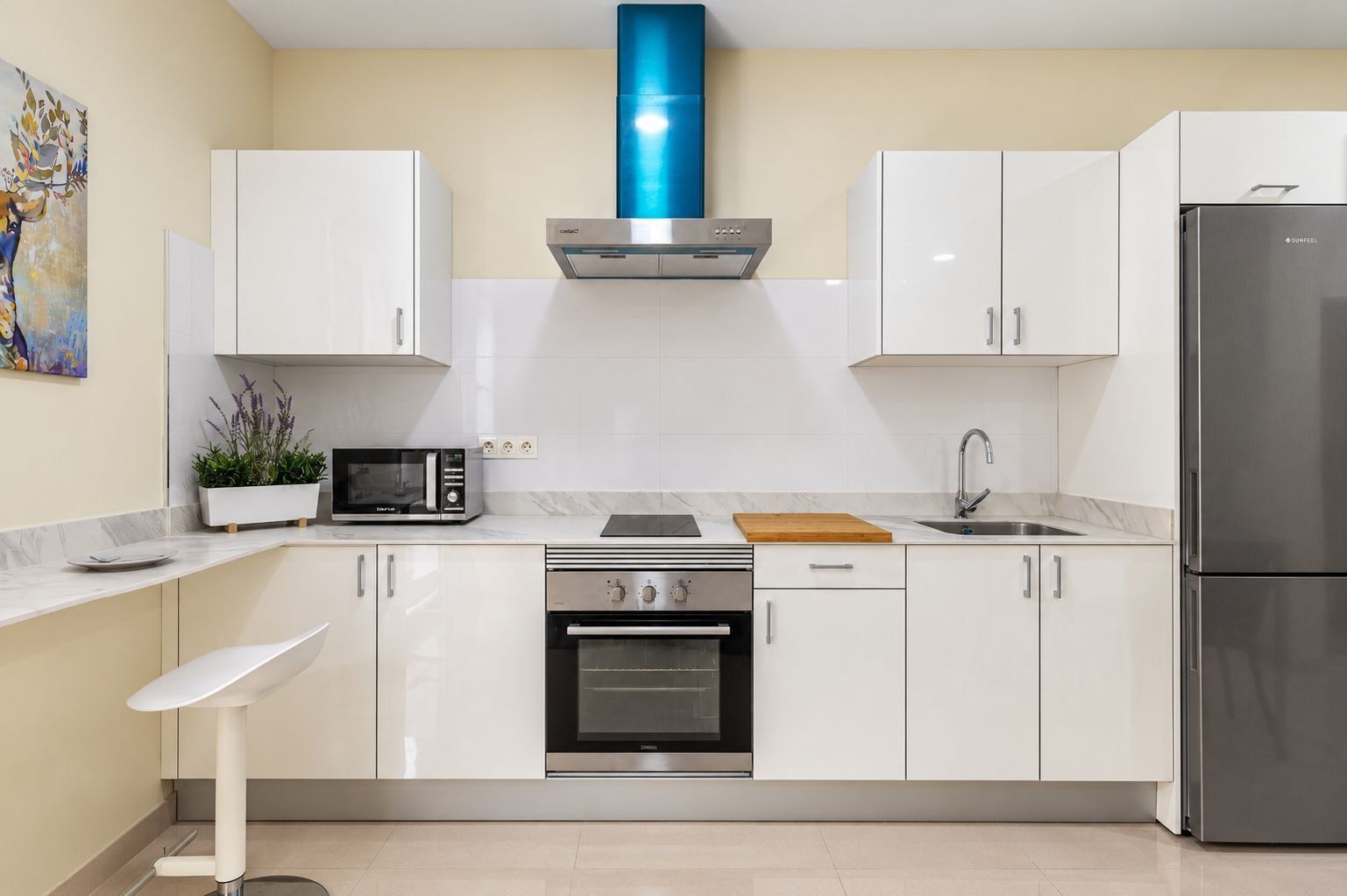A modern kitchen with white cabinets, a stainless steel refrigerator, a microwave, an oven, and a sink.