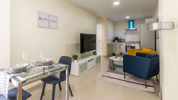 Eine moderne Wohnung mit Essbereich, Wohnzimmer mit Fernseher, Küche und kleinem Balkon.