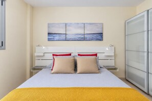 Quarto com cama, mesas de cabeceira, criado-mudo, um quadro sobre a cama e um guarda-roupa.
