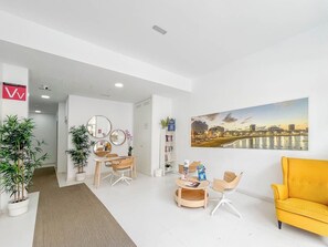 A modern hotel lobby with a seating area, a reception desk, and a large cityscape painting on the wall. - GuestReady - 03A Livian Suites Int 2 pax 3A (Las Palmas de Gran Canaria)