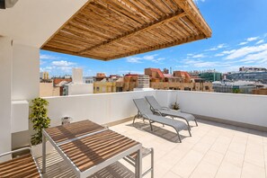 Terraço no telhado com pérgola de madeira, duas cadeiras de descanso, uma mesa e um vaso de planta.