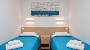 A hotel room with two beds, each with a blue bedspread and white pillows, a wooden nightstand, and a wall-mounted painting. - GuestReady - Alemania Villa Garden (San Bartolomé de Tirajana)