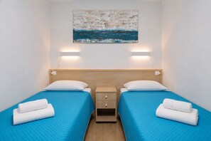 A hotel room with two beds, each with a blue bedspread and white pillows, a wooden nightstand, and a wall-mounted painting. - GuestReady - Alemania Villa Garden (San Bartolomé de Tirajana)