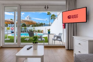 A hotel room with a pool view, a TV screen displaying 'GUEST READY', a remote control, a plant, and a white table. - GuestReady - Alemania Villa Garden (San Bartolomé de Tirajana)
