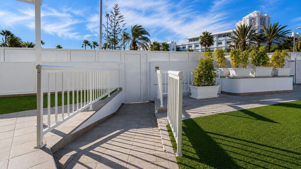 A gated outdoor area with a white fence, a paved walkway, and a well-maintained lawn. - GuestReady - Alemania Villa Garden (San Bartolomé de Tirajana)