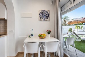 Ein Essbereich mit einem weißen Tisch, zwei Stühlen, einer Obstschale, einer Wasserflasche und einer Wanddekoration.