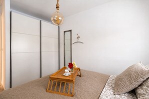Ein Schlafzimmer mit einem Bett, einem kleinen Holztisch mit Blumen in einer Vase, einer Hängelampe und einem Spiegel an der Wand.