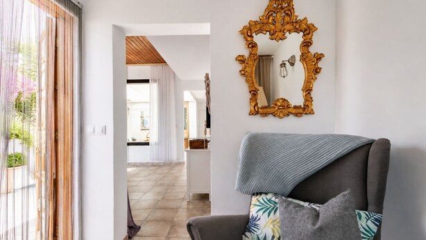 A modern living room with a grey sofa, a decorative mirror, and a view into the kitchen. - GuestReady - Casa Dey with terrace (Telde)