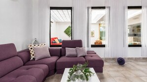 A modern living room with a sectional sofa, a coffee table with decorative items, and large windows with sheer curtains. - GuestReady - Casa Dey with terrace (Telde)