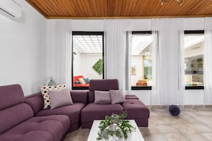 Ein modernes Wohnzimmer mit einem Ecksofa, einem Couchtisch mit Dekoration und großen Fenstern mit durchsichtigen Vorhängen.
