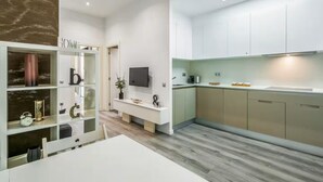 Una cocina moderna con armarios blancos, horno integrado y televisor de pantalla plana.
