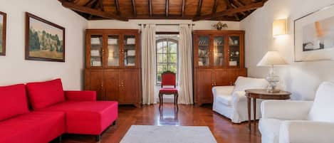 Une pièce avec un canapé rouge, des fauteuils blancs, un meuble en bois et une chaise rouge.