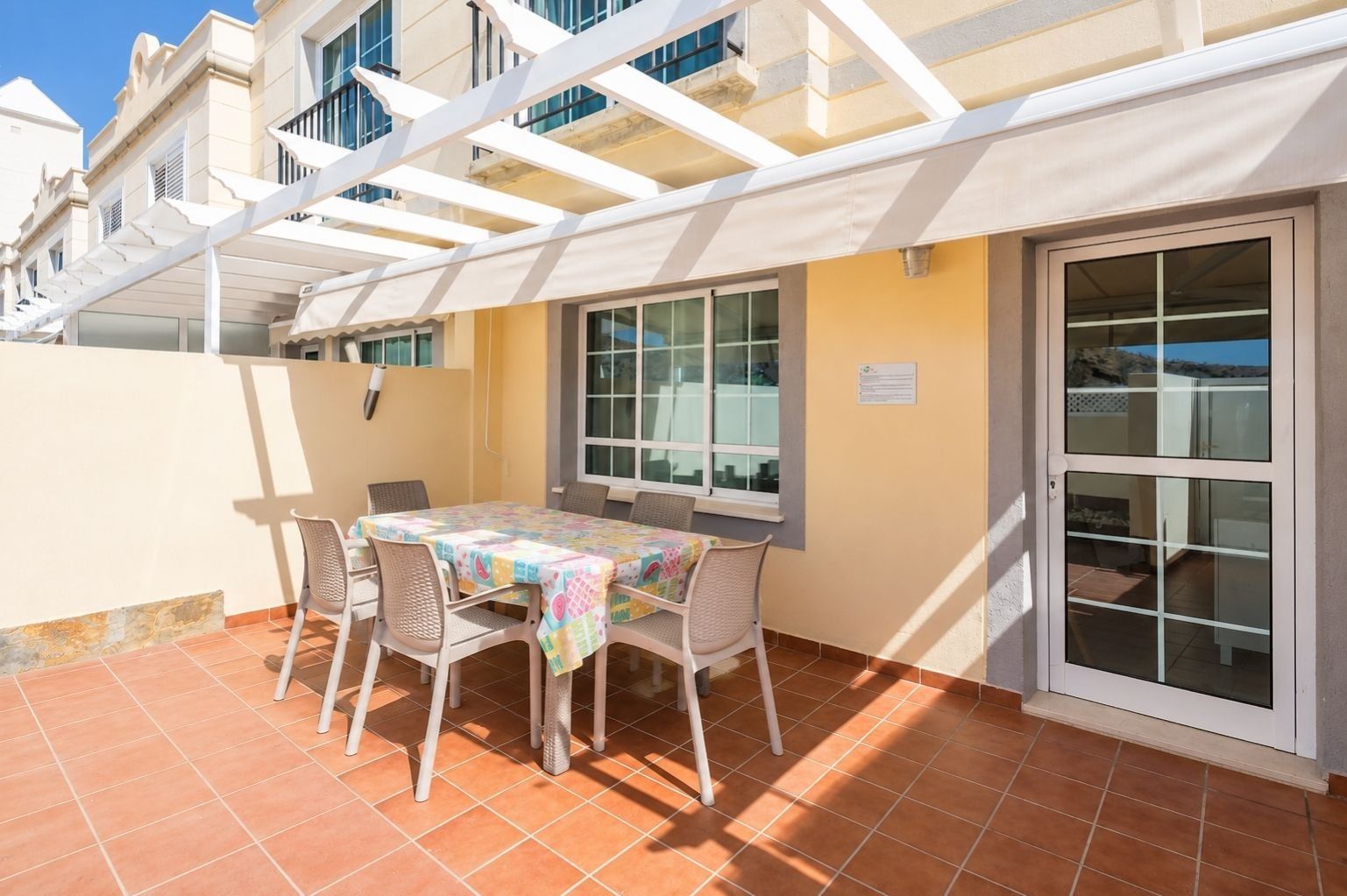 Une terrasse avec une table et des chaises, un espace abrité et une porte-fenêtre coulissante.