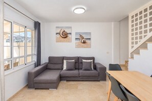 A modern living room with a sectional sofa, a wooden dining table, and artwork on the walls. - GuestReady - Puerto Rico Family Retreat (Las Palmas de Gran Canaria)