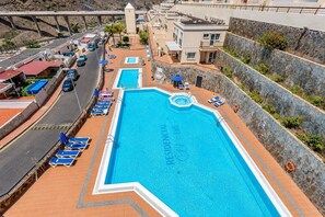 A large swimming pool with a stone wall and a view of the surrounding area. - GuestReady - Puerto Rico Family Retreat (Las Palmas de Gran Canaria)