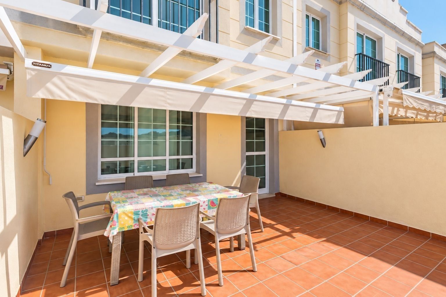 A covered outdoor patio with a table and chairs, a window, and a building in the background.