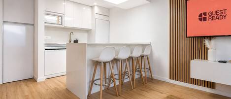 Una cocina moderna con armarios blancos, horno empotrado y una barra con taburetes.