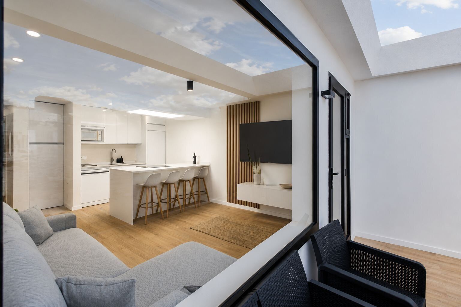 A modern kitchen with a central island, bar stools, and a dining area with a sofa.