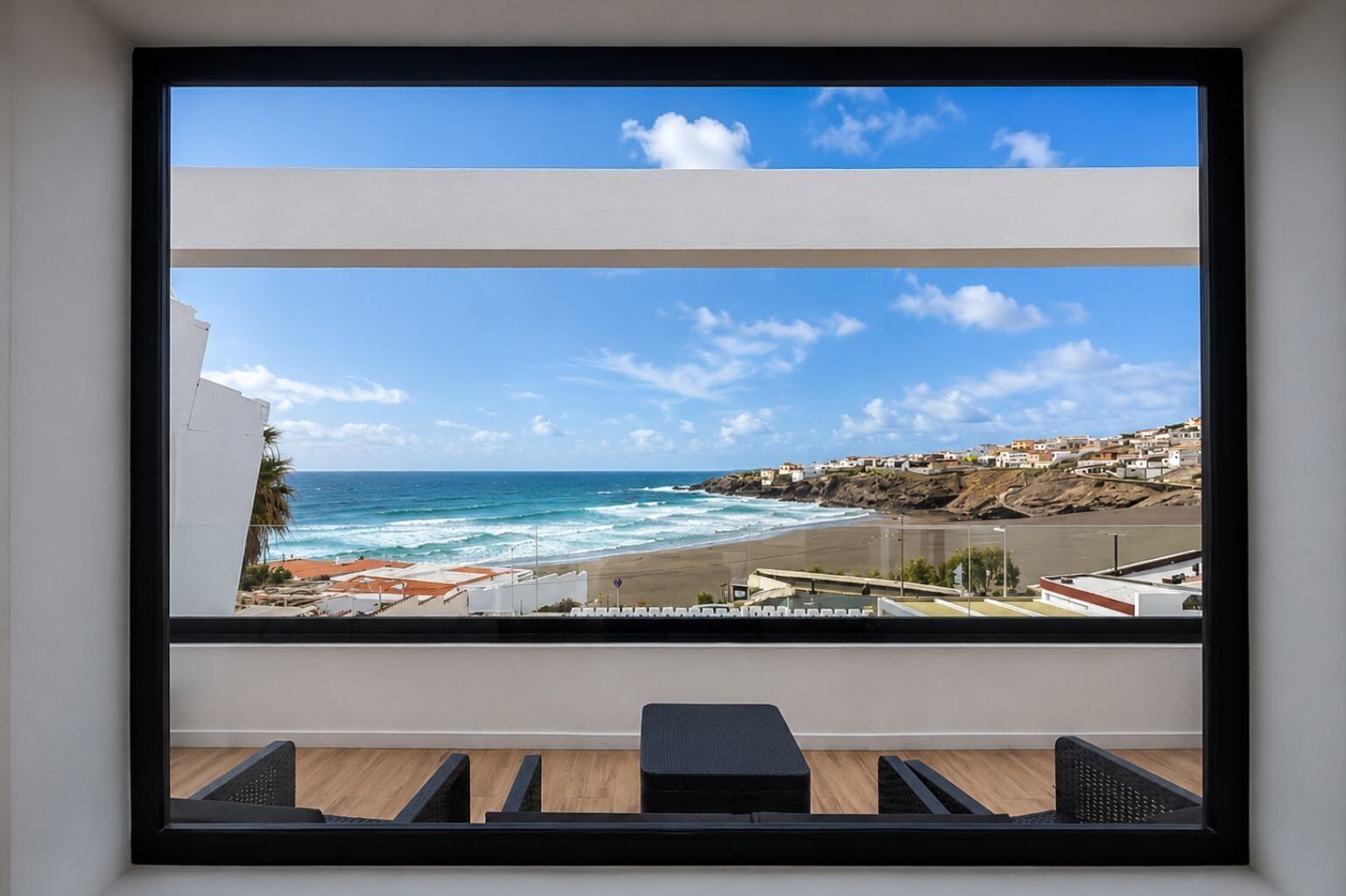 Een kamer met een groot raam met uitzicht op een strand en een kustplaats.
