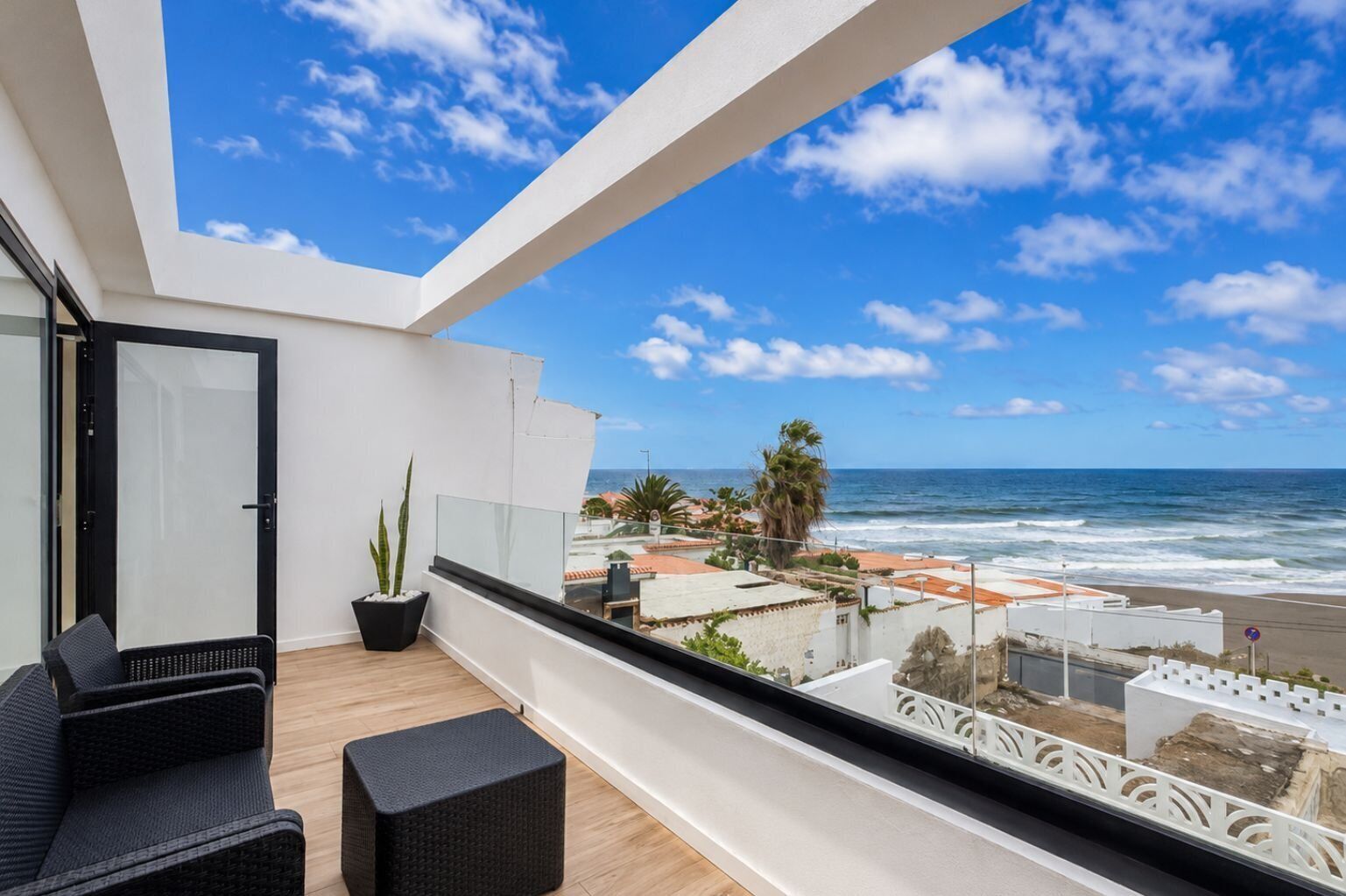 A balcony with a view of the ocean, a door, and a seating area with a potted plant.