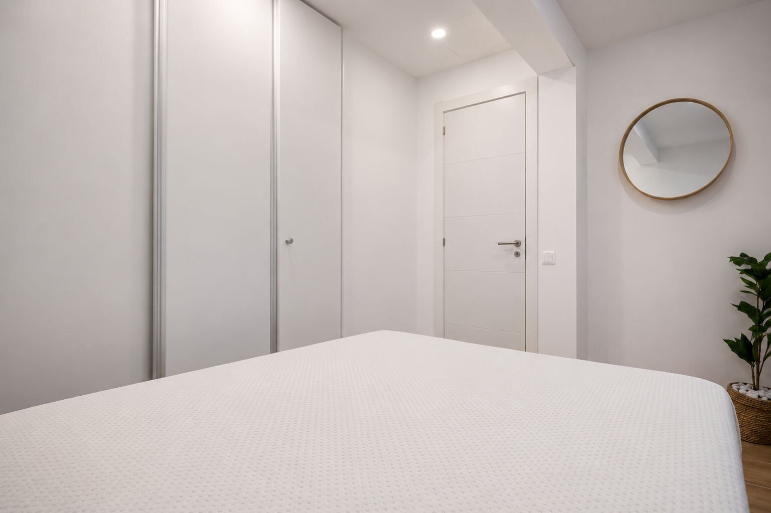 Une chambre à coucher avec un lit, une armoire, une porte et un miroir rond accroché au mur.