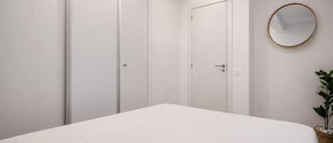 A bedroom with a bed, a wardrobe, a door, and a round mirror on the wall.