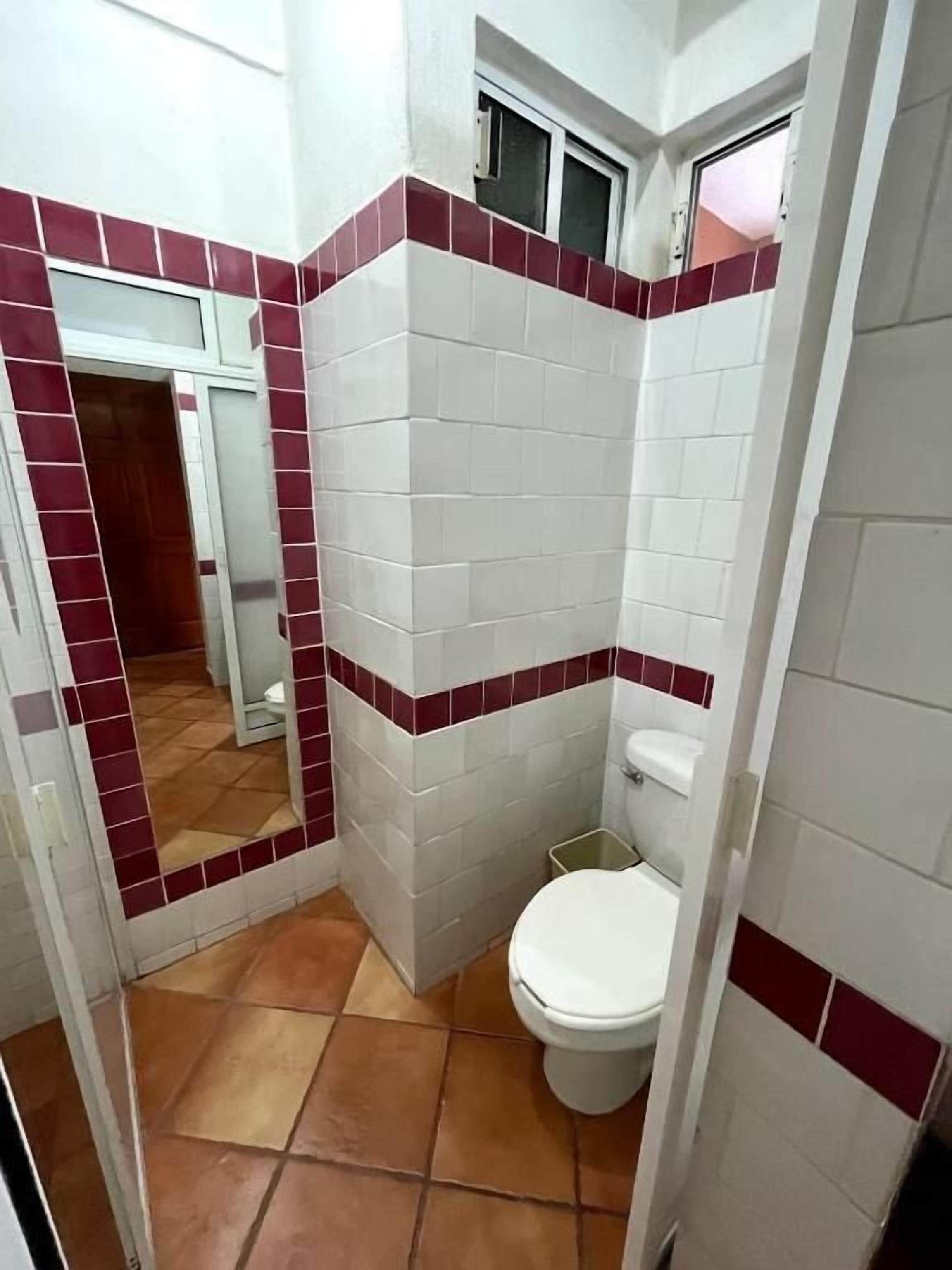 A bathroom with white and red tiles, a white toilet, and a visible door leading to another room.