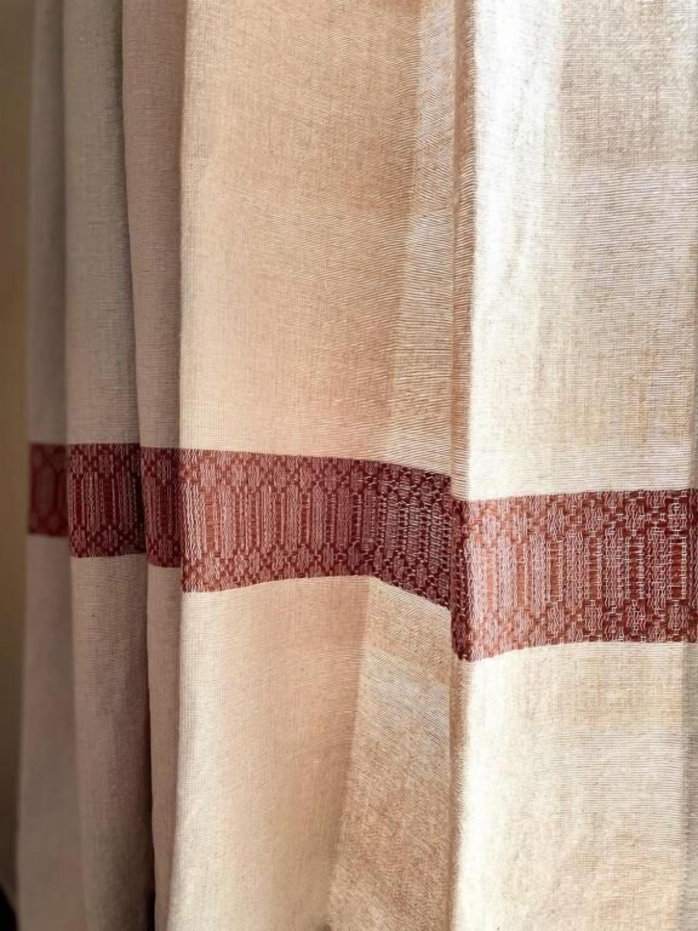 A close-up of a curtain with a textured fabric and a patterned trim.