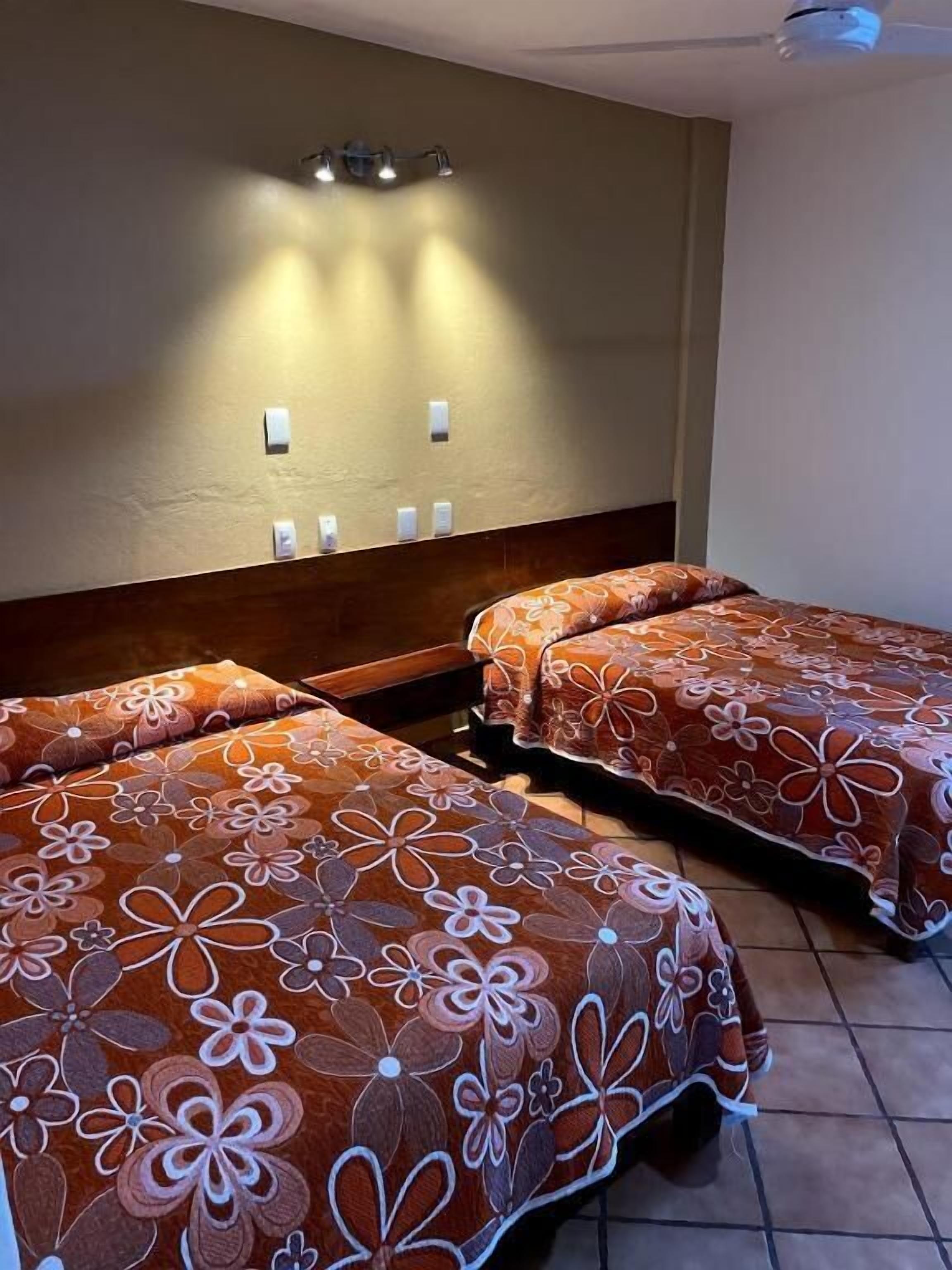 A hotel room with two beds, a wooden headboard, wall-mounted light fixtures, and a tiled floor.