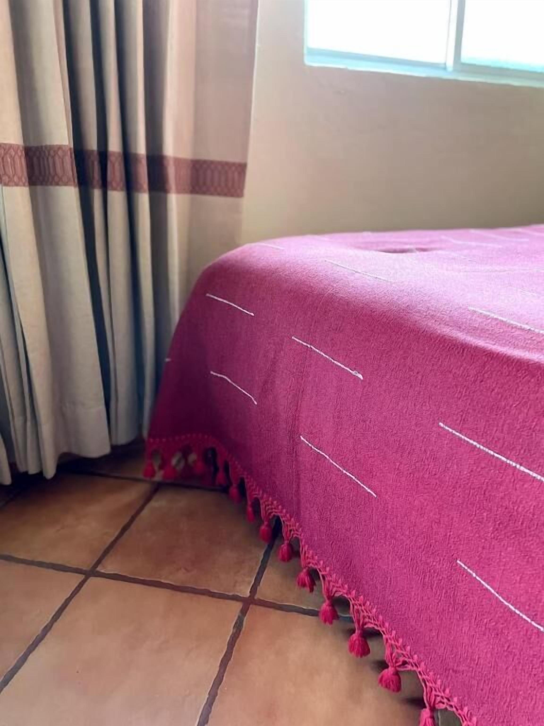 A room with a bed covered in a pink blanket, curtains, and a tiled floor.